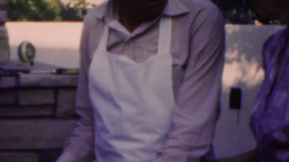 The final 1949 Seaside, New Jersey frame shows the apron-wearing man beside a masonry outdoor cooking area, with the woman cropped along the right edge.