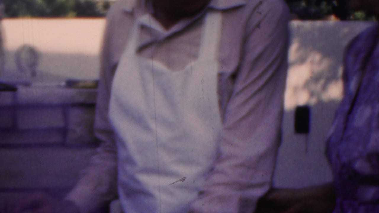 In Seaside, New Jersey home-movie footage from 1949, an older man in a light shirt and white apron stands beside an older woman in a patterned dress on a porch.