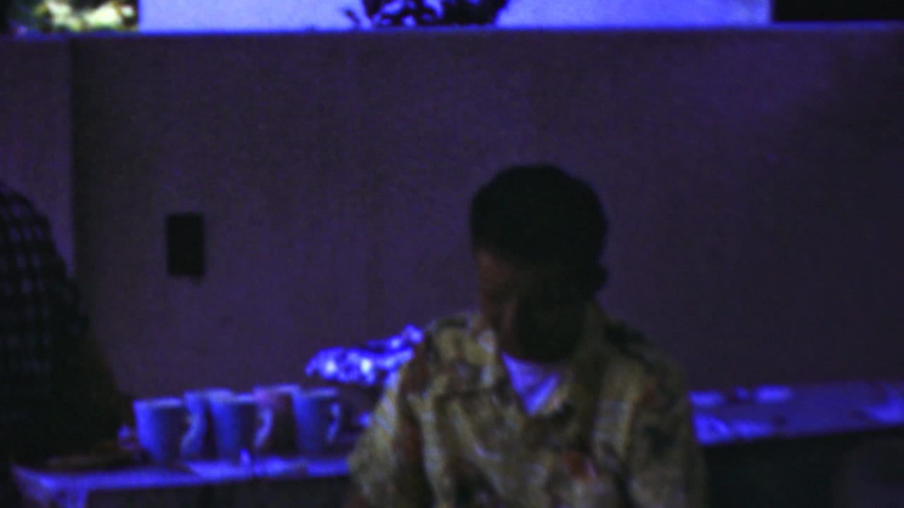 Two young men sit near cups and a table in strong blue lighting.