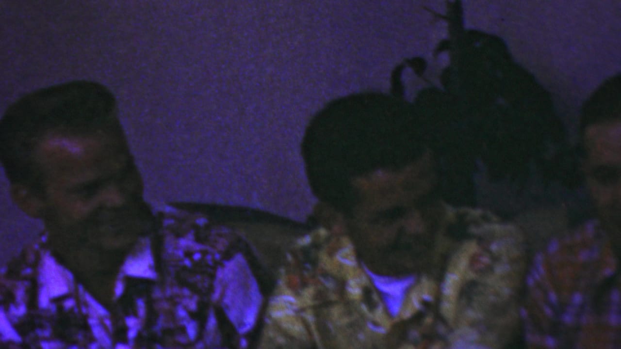 Three adult men face each other in conversation beside dark vertical posts.