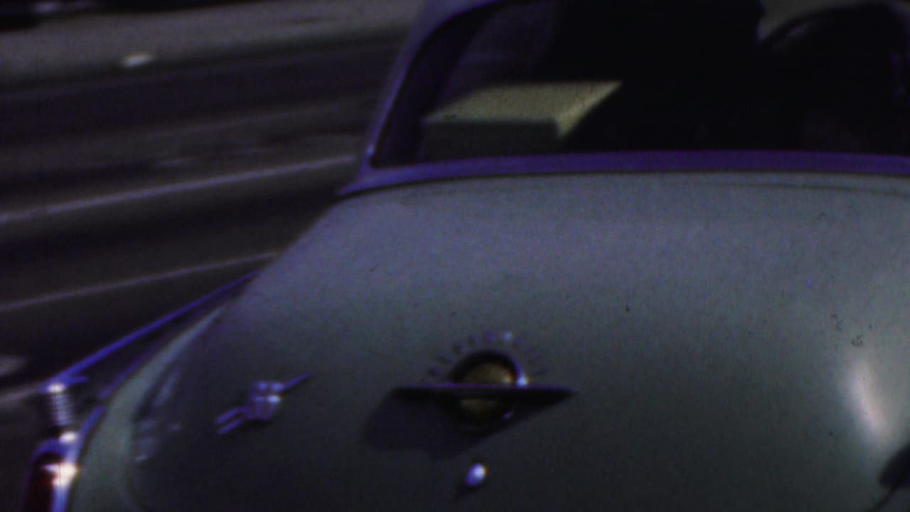 Close rear view of a pale vintage sedan with chrome trim traveling along a street in the supplied 1949 Seaside, New Jersey home-movie context.