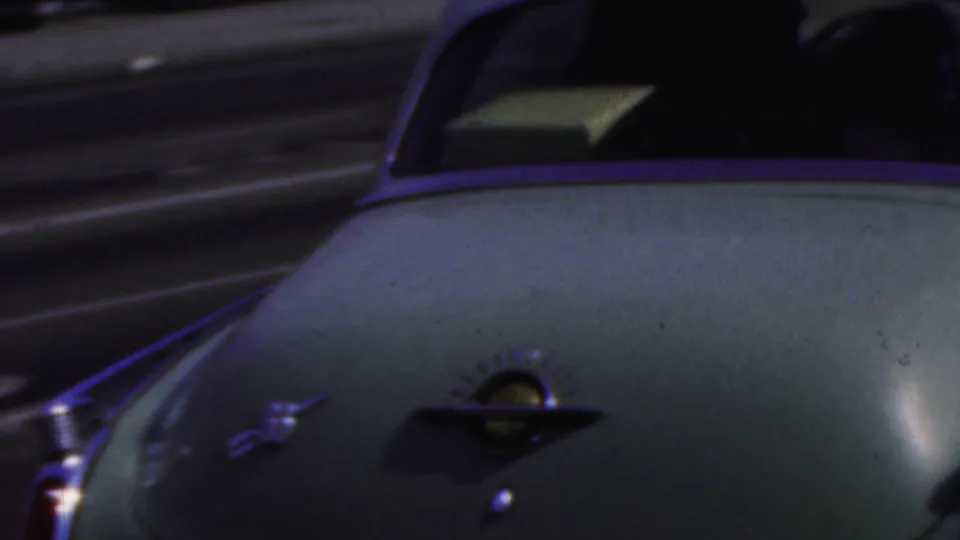 Close rear view of a pale vintage sedan with chrome trim traveling along a street in the supplied 1949 Seaside, New Jersey home-movie context.