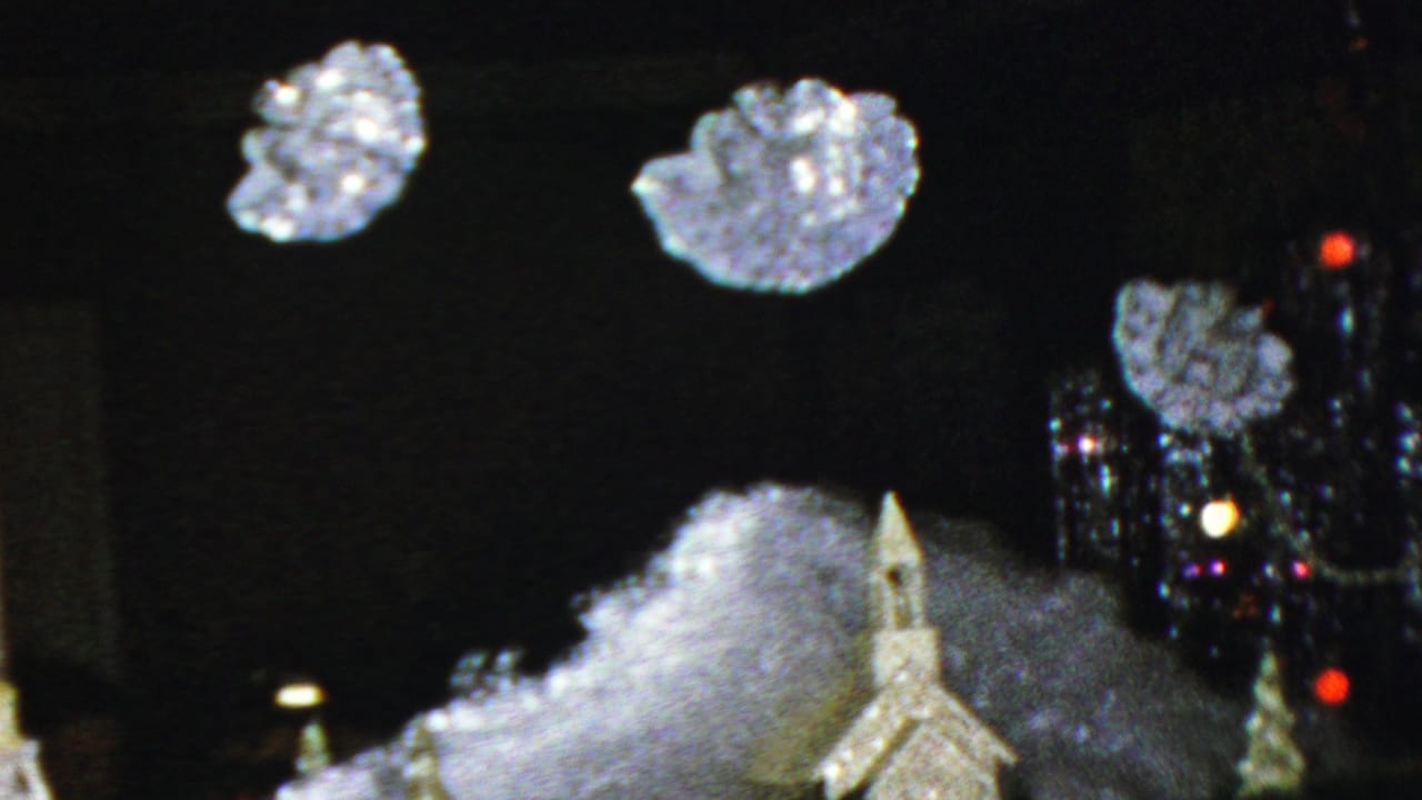Miniature chapel display with artificial snow and a lit decorated tree beside suspended snowflake ornaments.