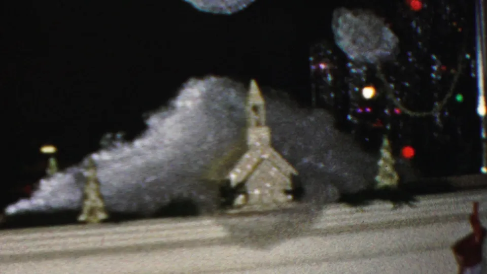 1949 Seaside, New Jersey 8mm frame showing a miniature chapel on artificial snow, a small decorated tree, and a suspended snowflake ornament near a mantel.