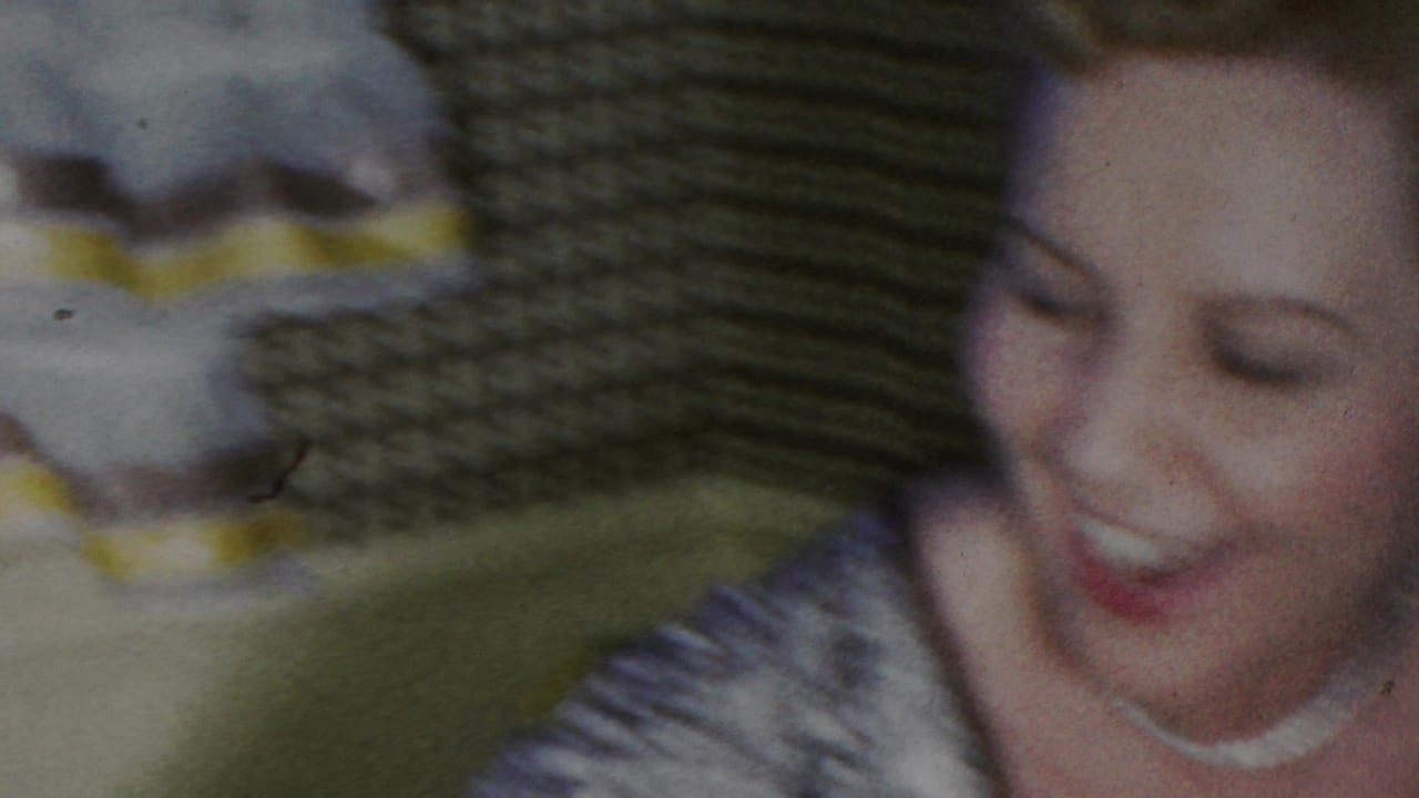 Smiling pregnant woman in a patterned dress appears in a 1949 Seaside, New Jersey home-movie frame, with domestic furnishings and soft motion blur around her.