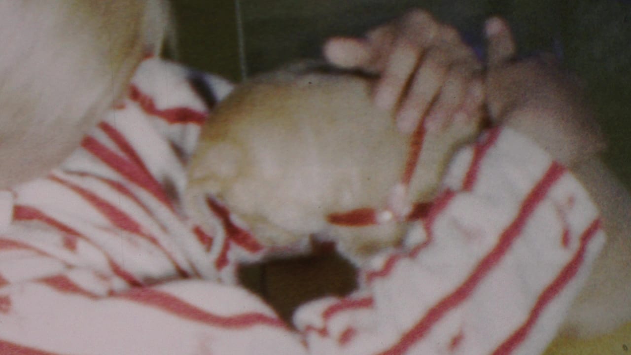 In 1949 Seaside, New Jersey home-movie footage, a young person in a red-and-white striped shirt cradles a small light-colored puppy in a close handheld interior shot.