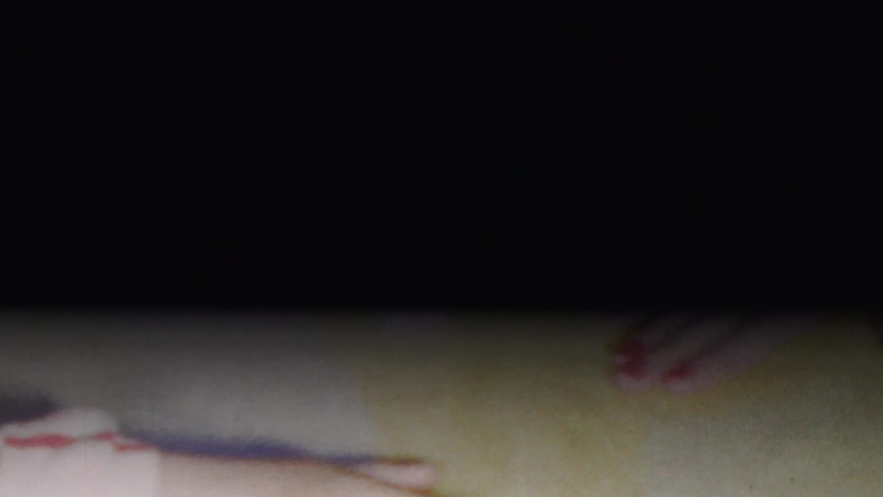 A mostly underexposed 8mm frame shows only partial red-and-white striped clothing and a small foot at the edge, suggesting the handheld camera has drifted away from the puppy.