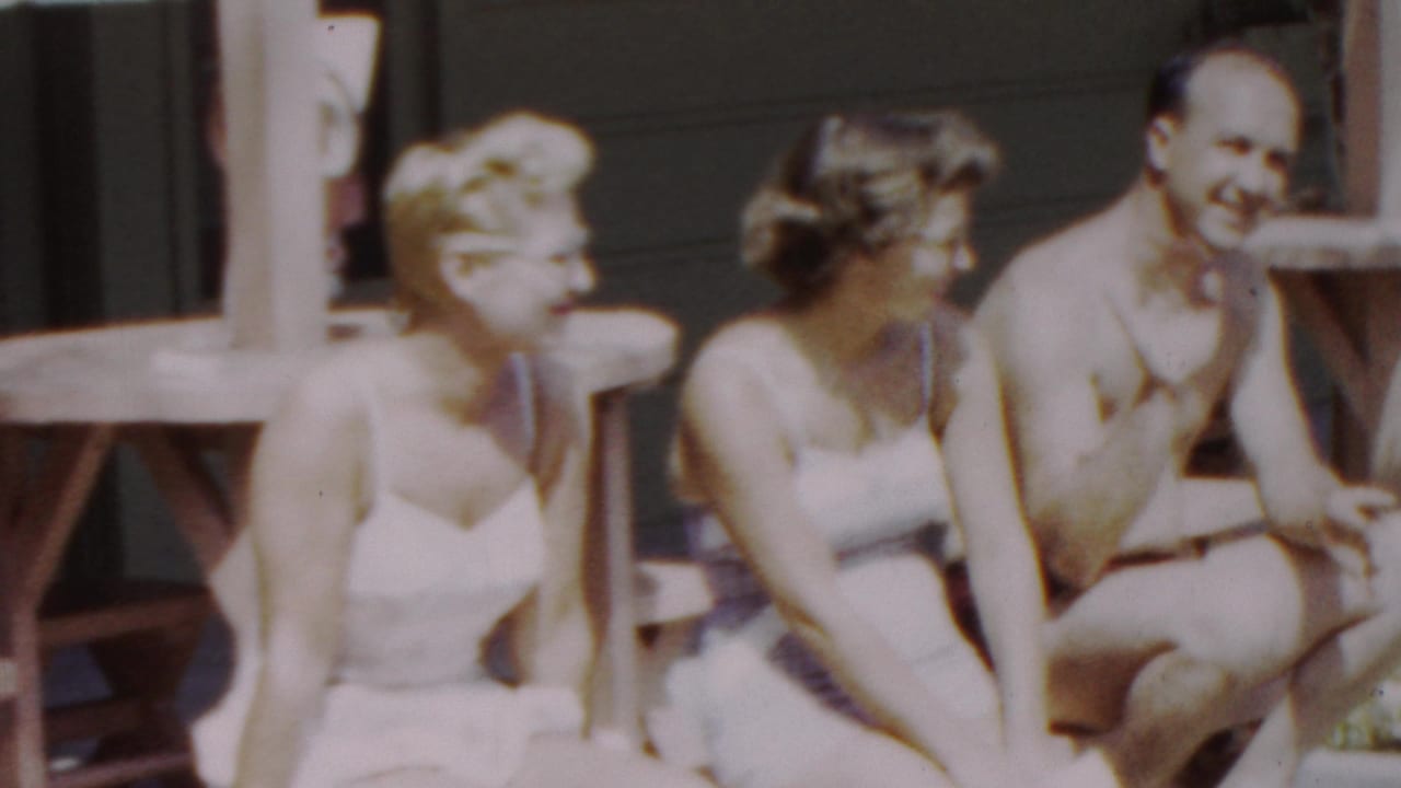 Two women and a man in swimwear sit together, with the man turned toward the camera.