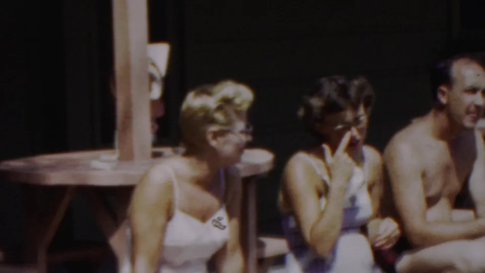 At the end of the clip, the seated poolside group is visible again, with one woman raising a hand near her face and the man turned slightly toward the camera.