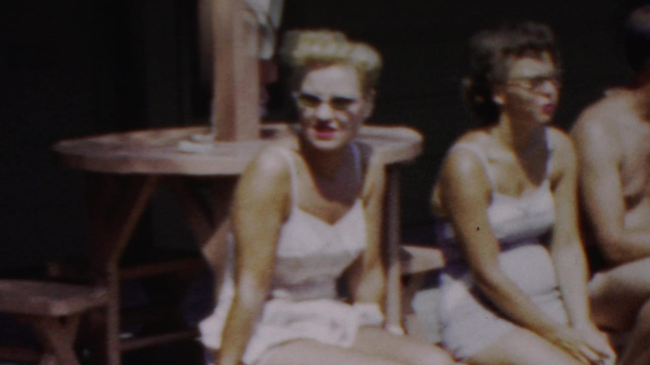 A woman in a white swimsuit sits on a bench while other adults sit nearby.