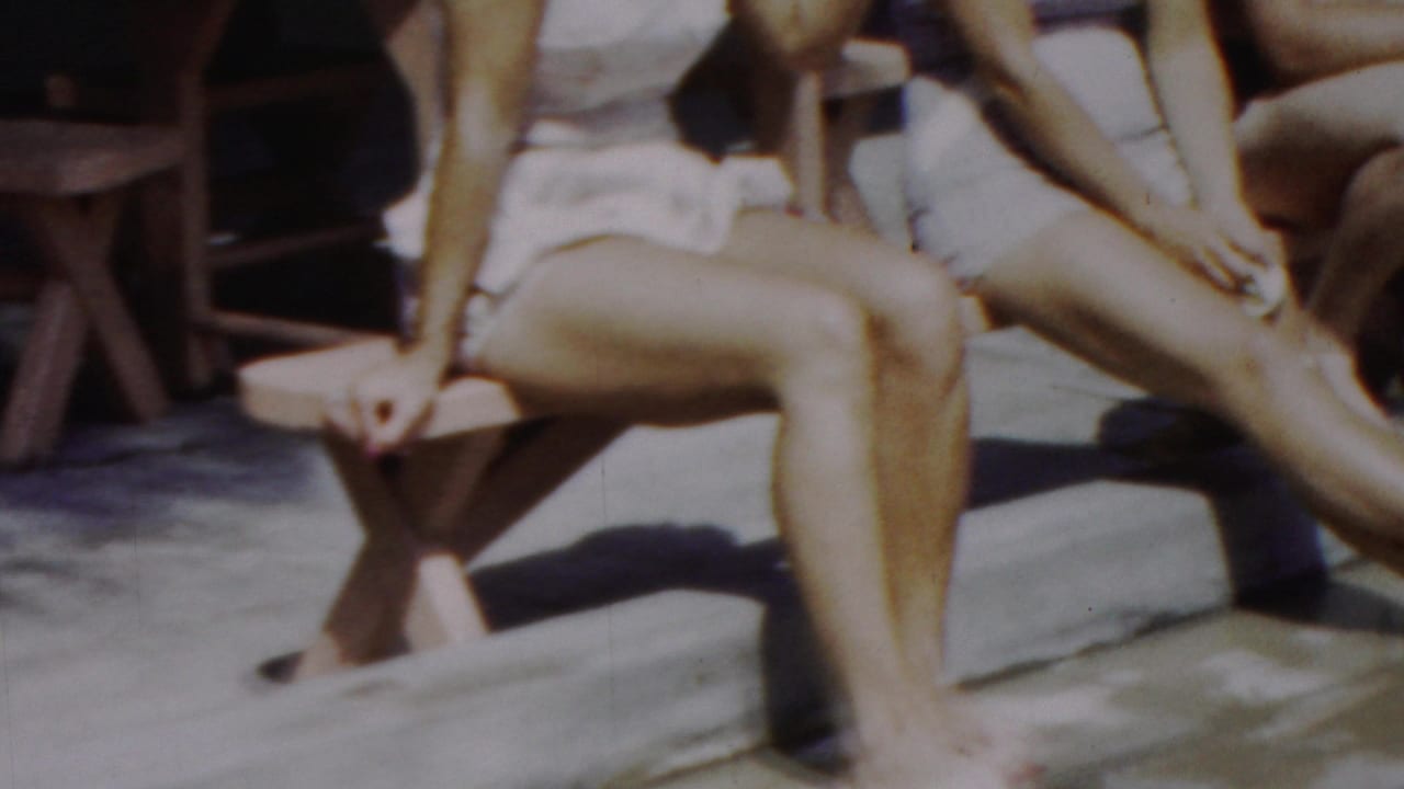 Adults in mid-century swimwear sit on wooden benches in a sunny poolside setting, consistent with the supplied 1949 Seaside, New Jersey home-movie metadata.