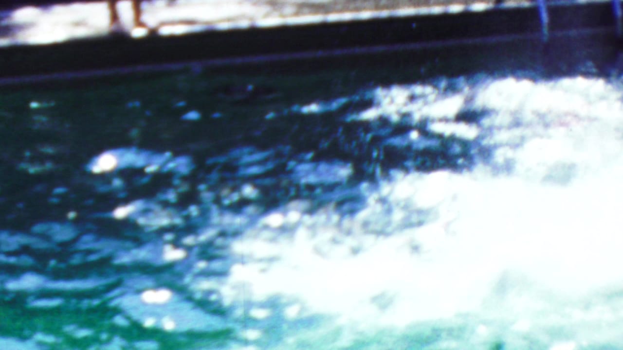In Seaside, New Jersey 1949 home-movie footage, bright splashing pool water fills the frame as an adult swimmer is mostly submerged near the surface.