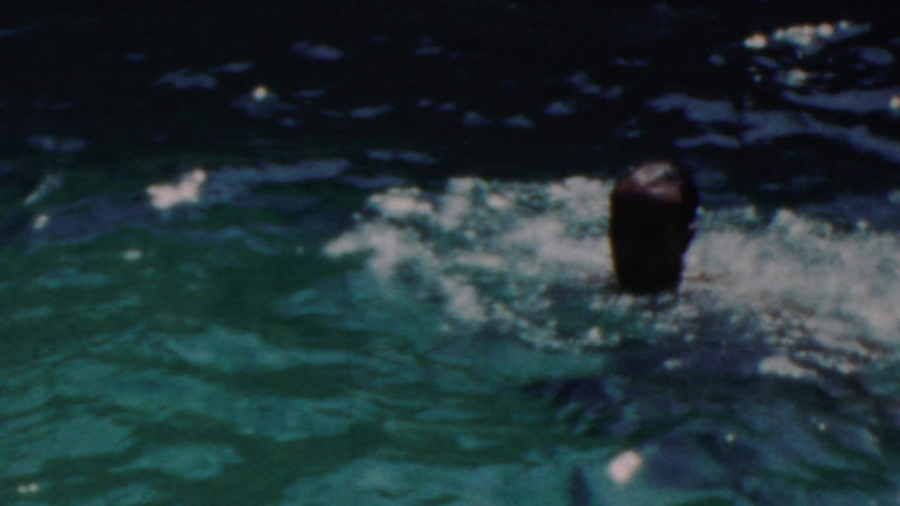 An adult man surfaces in a resort pool in the supplied 1949 Seaside, New Jersey footage, with rippled green water and sunlit reflections around him.