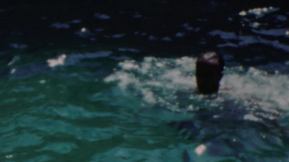 An adult man surfaces in a resort pool in the supplied 1949 Seaside, New Jersey footage, with rippled green water and sunlit reflections around him.
