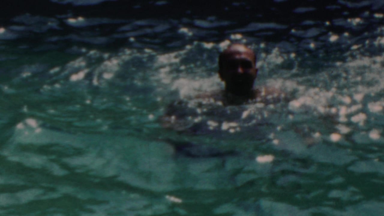 The swimmer faces the camera from chest-deep water in the 1949 Seaside, New Jersey pool scene, with softened focus and bright ripples across the frame.