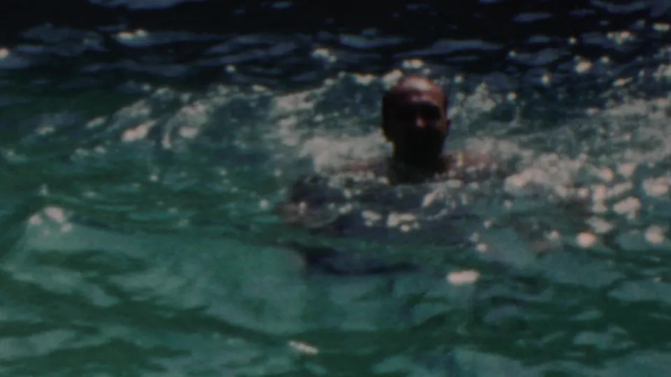 The swimmer faces the camera from chest-deep water in the 1949 Seaside, New Jersey pool scene, with softened focus and bright ripples across the frame.