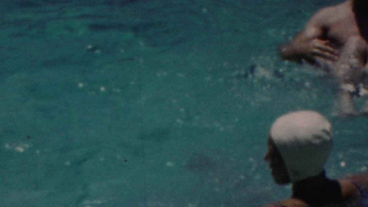A woman in a white swim cap and dark swimsuit watches in the pool while another swimmer splashes nearby in 1949 Seaside, New Jersey home-movie footage.