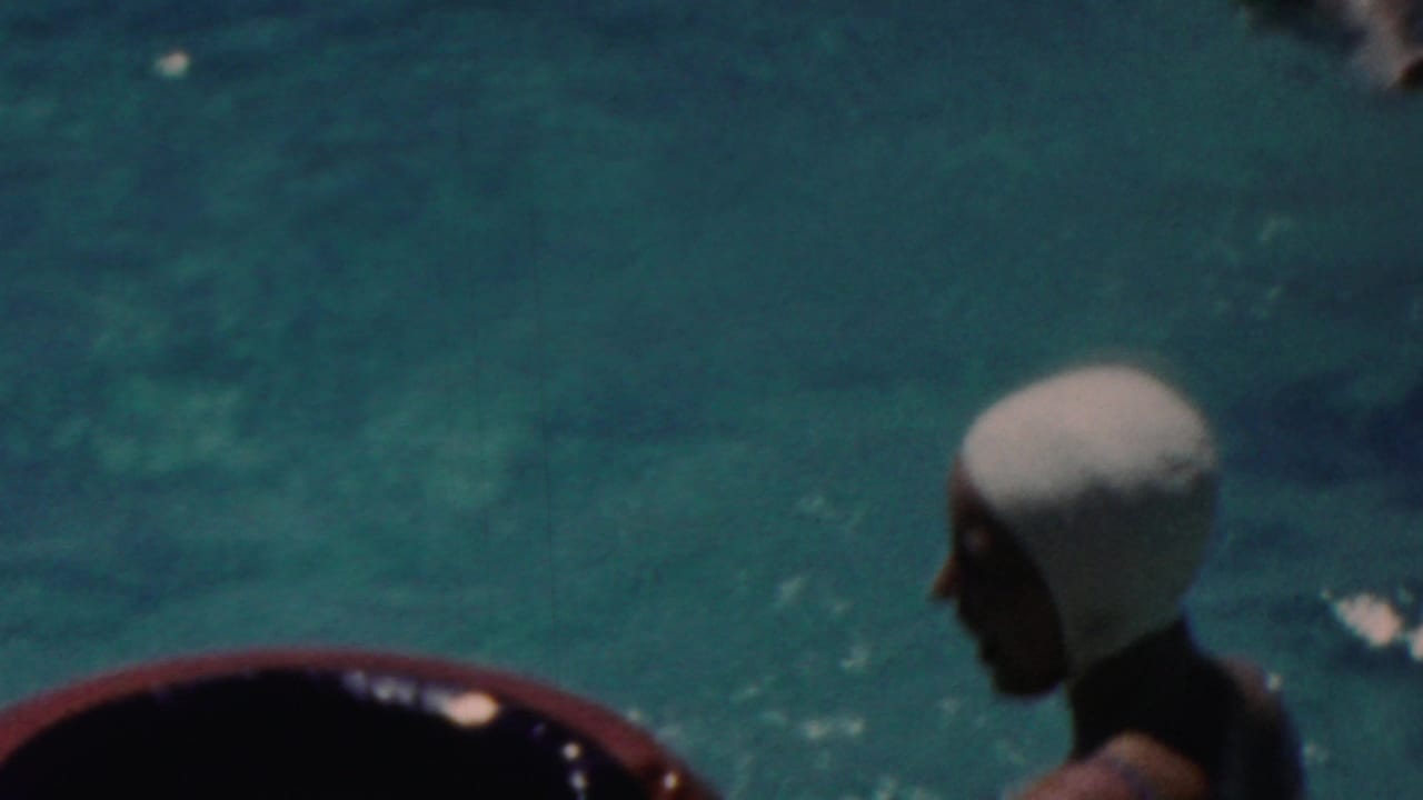 A woman in a white swim cap is seen in profile beside the rounded pool edge, with blue-green water behind her in the 1949 Seaside, New Jersey pool footage.