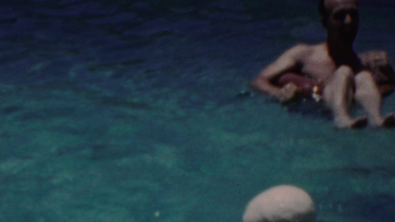 In Seaside, New Jersey, 1949 home-movie footage, a man floats on a red inner tube in blue-green pool water with sunlit ripples around him.