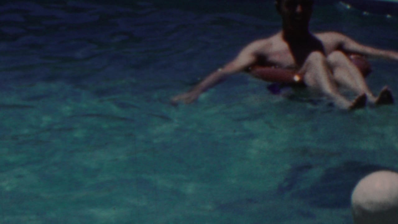 Man seated on a red inner tube with one arm extended over the pool water.