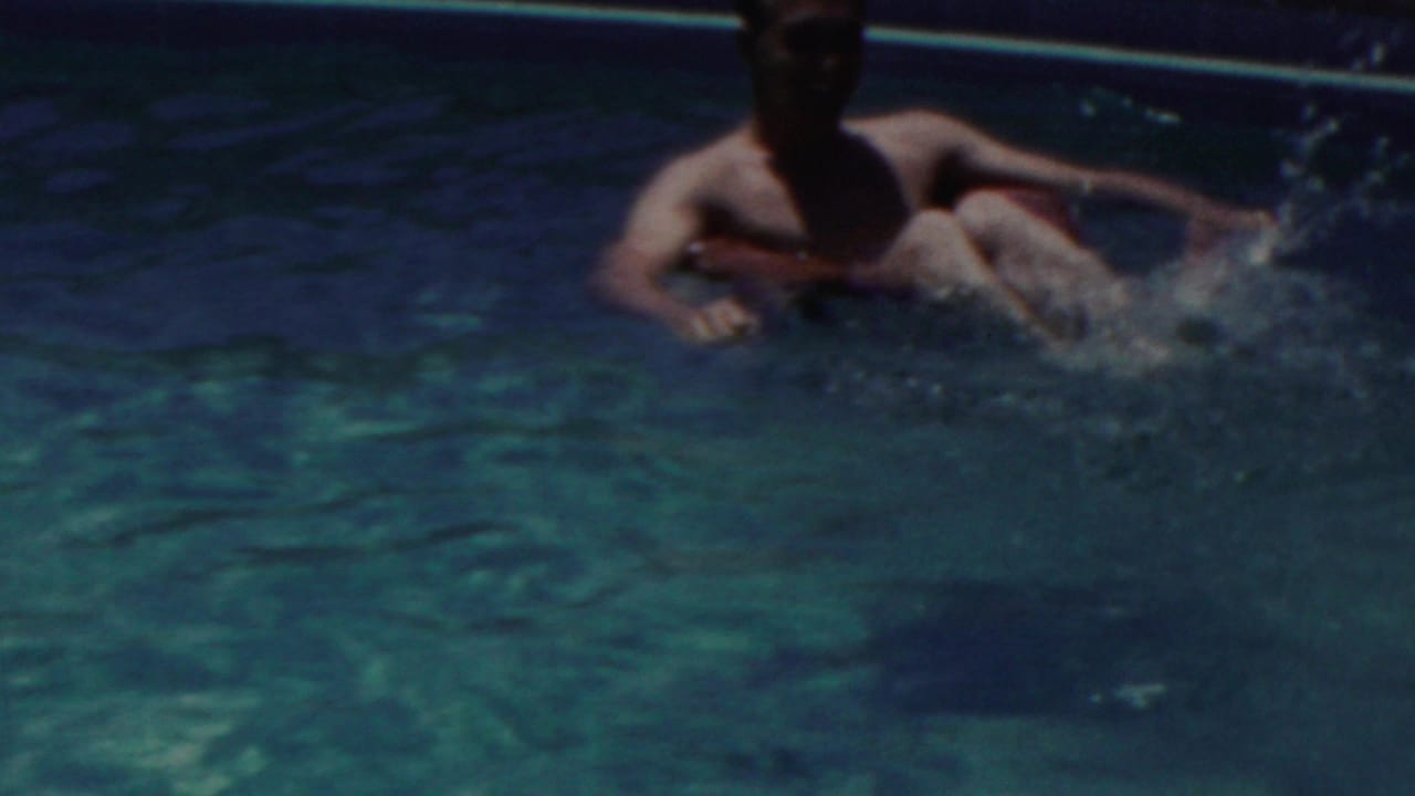 A shirtless swimmer appears in turquoise pool water in this 1949 Seaside, New Jersey home-movie frame, with splashes and the pool edge visible.