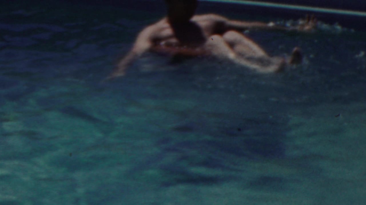 Man floating in a pool on a red inner tube with legs raised.