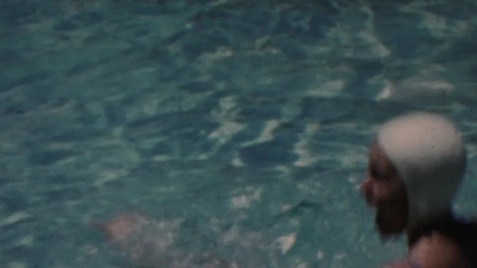 A woman in a white swim cap and dark swimsuit moves through turquoise pool water, seen from the side in a 1949 Seaside, New Jersey home-movie frame.