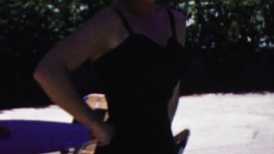 An adult woman in a dark swimsuit stands with hands on hips beside visible pool water and bright concrete in the 1949 Seaside, New Jersey home-movie footage.