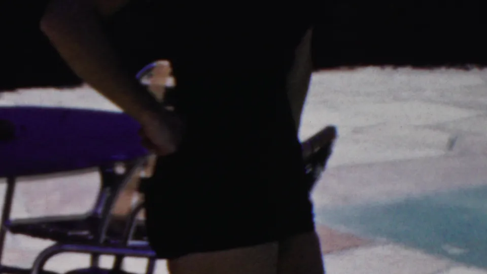 In 1949 Seaside, New Jersey home-movie footage, a woman in a dark strapless swimsuit is framed from torso to thighs near metal patio chairs and sunlit paving.