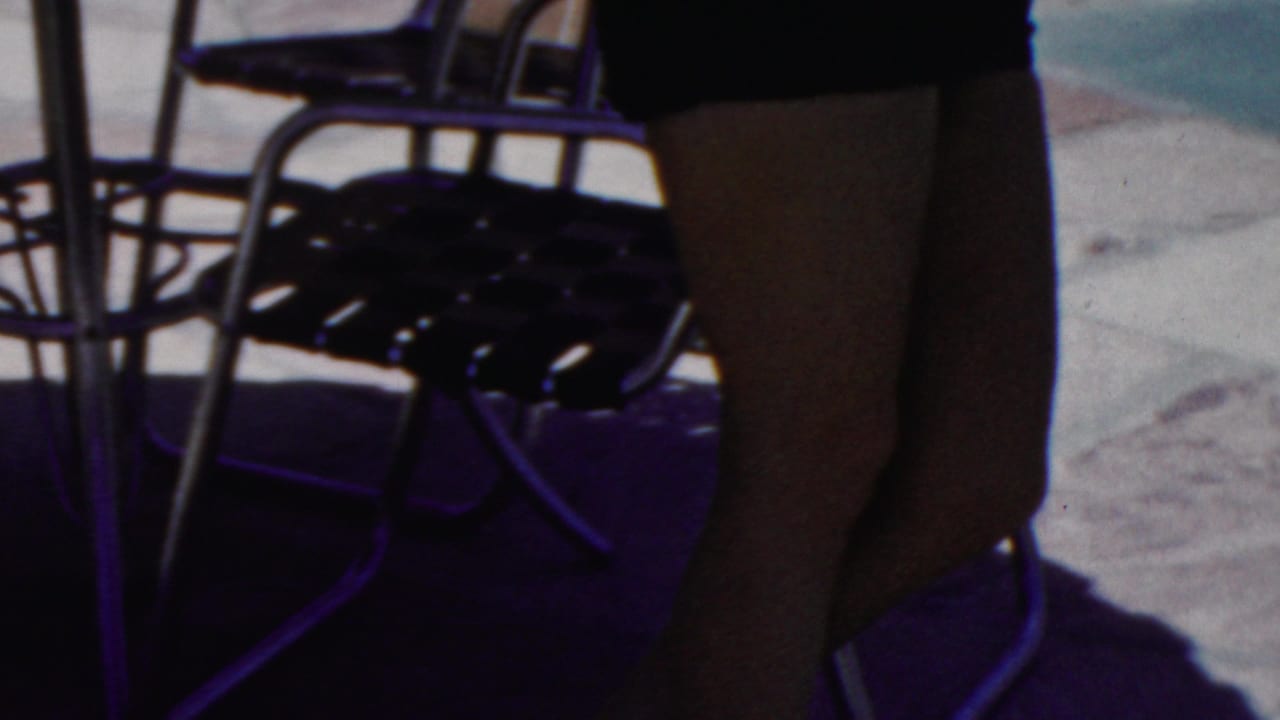 Close poolside view shows a woman's legs near metal chairs and bright paving.