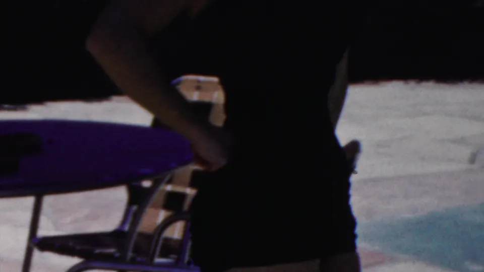 The home-movie frame shows a woman in a dark strapless swimsuit posing with her hand on her hip beside a lounge chair and sunlit poolside paving in Seaside, New Jersey.