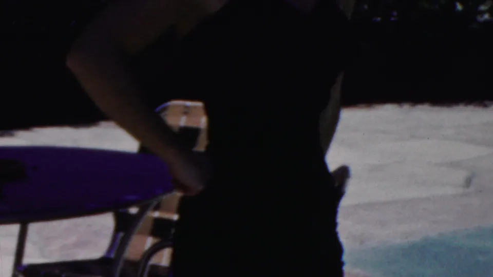 A shadowed 1949 Seaside, New Jersey frame shows a close poolside view of a woman in a dark swimsuit with a lounge chair, pale paving, and blue-green pool color nearby.