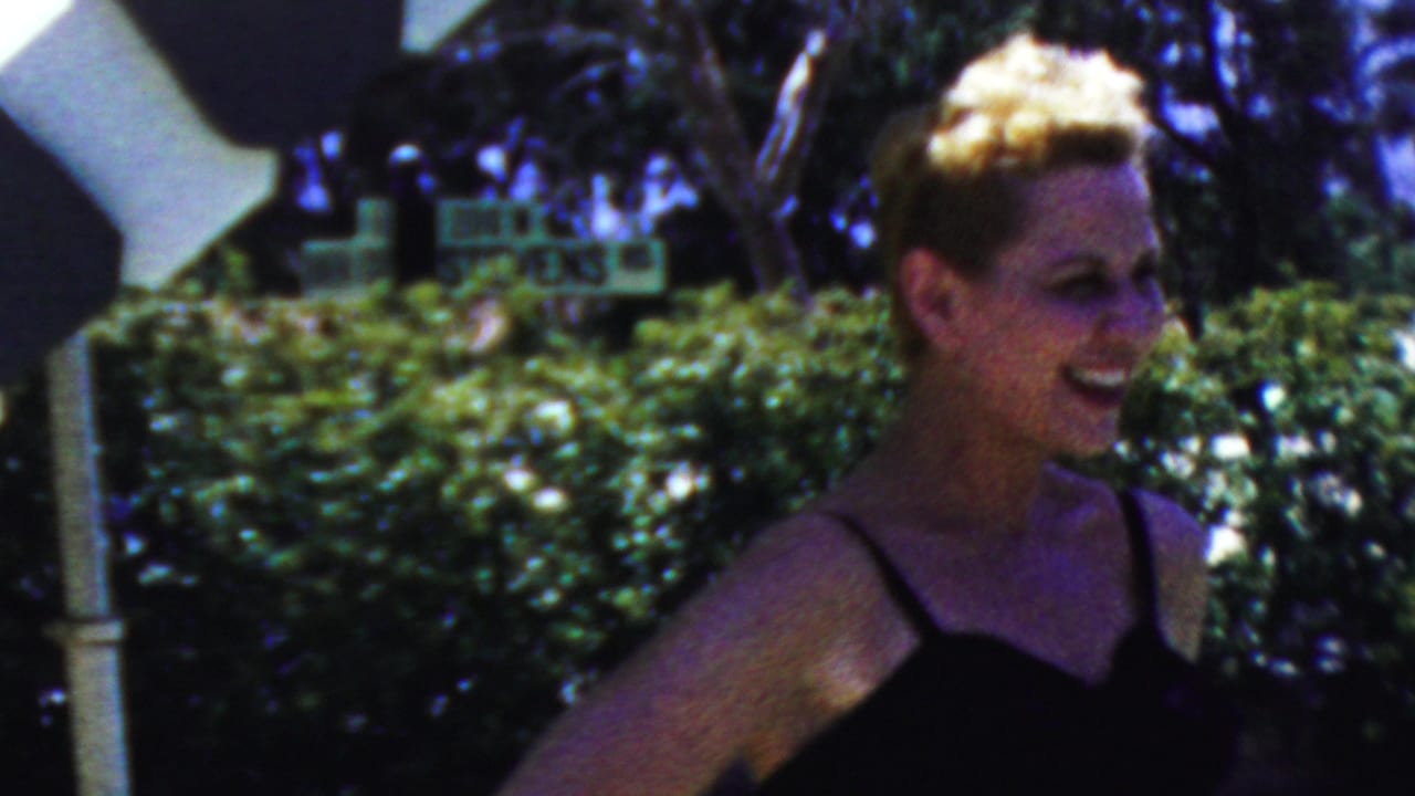A smiling woman in a dark dress stands outdoors near hedges and a white post in 1949 Seaside, New Jersey home-movie footage.