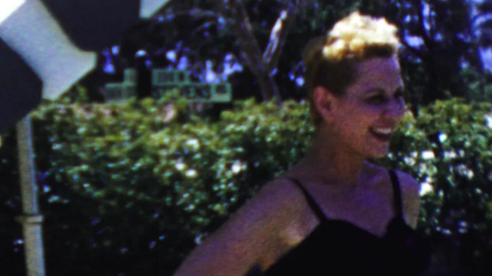 A smiling woman in a dark dress stands outdoors near hedges and a white post in 1949 Seaside, New Jersey home-movie footage.