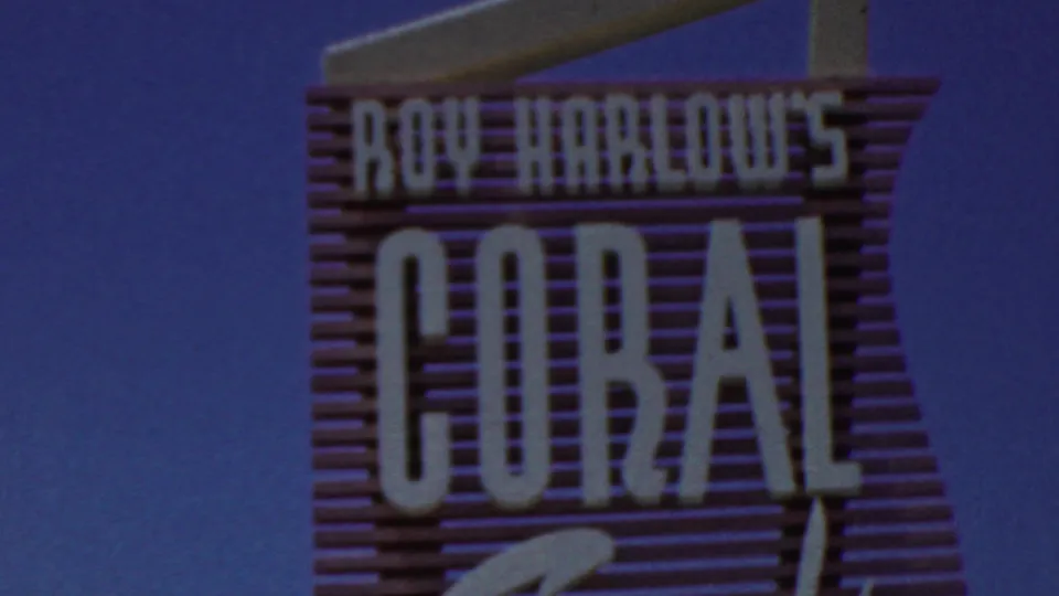 The frame shows a closer view of the "Roy Harlow's Coral" sign, with large white letters on a pink structure against the sky.