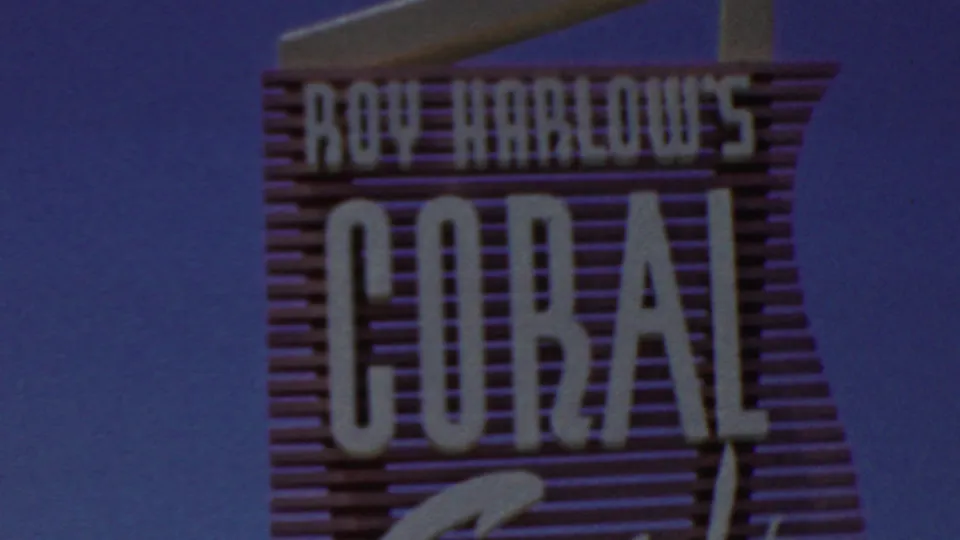 1949 8mm frame from Seaside, New Jersey showing the upper portion of the Roy Harlow's Coral Sands sign with block lettering and cursive script against a deep blue sky.