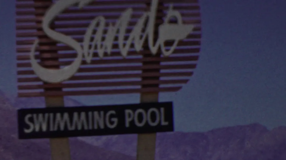 1949 Seaside, New Jersey home-movie frame showing the Coral Sands sign with its separate Swimming Pool marker beneath, set against blue sky and distant silhouettes.