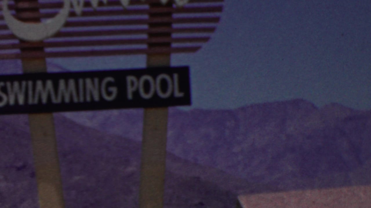 A 1949 8mm frame, identified by metadata as Seaside, New Jersey, showing part of a swimming pool sign and its striped support against distant purple-toned mountains.