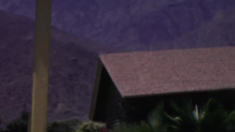 A color 8mm frame from the supplied 1949 clip showing a sloped building roof, palm fronds, a vertical post, and distant mountains under a purple cast.
