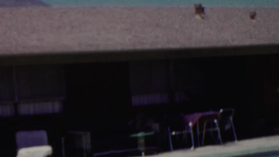 1949 Seaside, New Jersey frame showing a backyard pool edge, patio chairs, a shaded house facade, dark windows, and roof vents above.