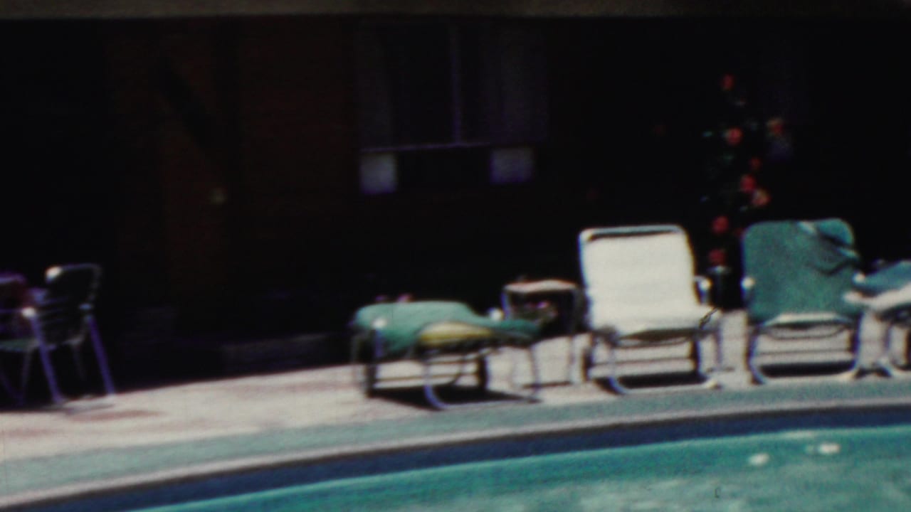 White and green lounge chairs arranged along the pool deck near planting.