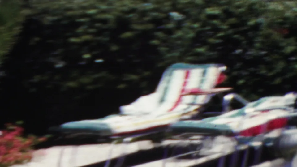 Striped mid-century lounge chairs sit on a concrete patio before leafy hedges and flowers in the supplied 1949 Seaside, New Jersey home-movie scene.