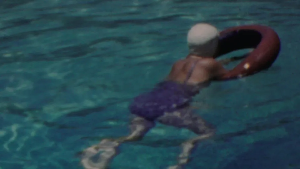 In the later pool frame, the woman paddles away from the camera with a red inner tube, her swim cap and dark swimsuit visible against rippling turquoise water.