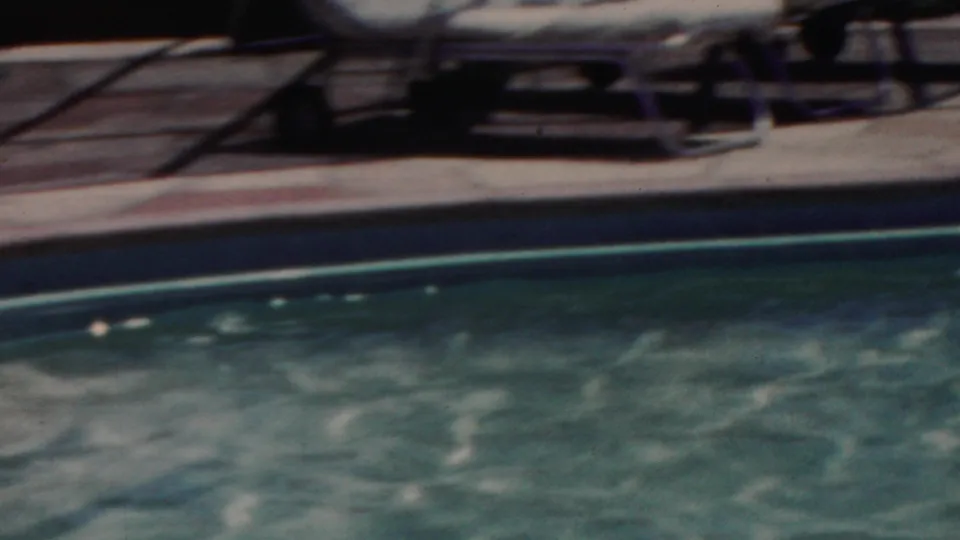 1949 Seaside, New Jersey pool frame showing rippling water, dark pool edging, a sunlit deck, and vintage lounge chairs in the background.