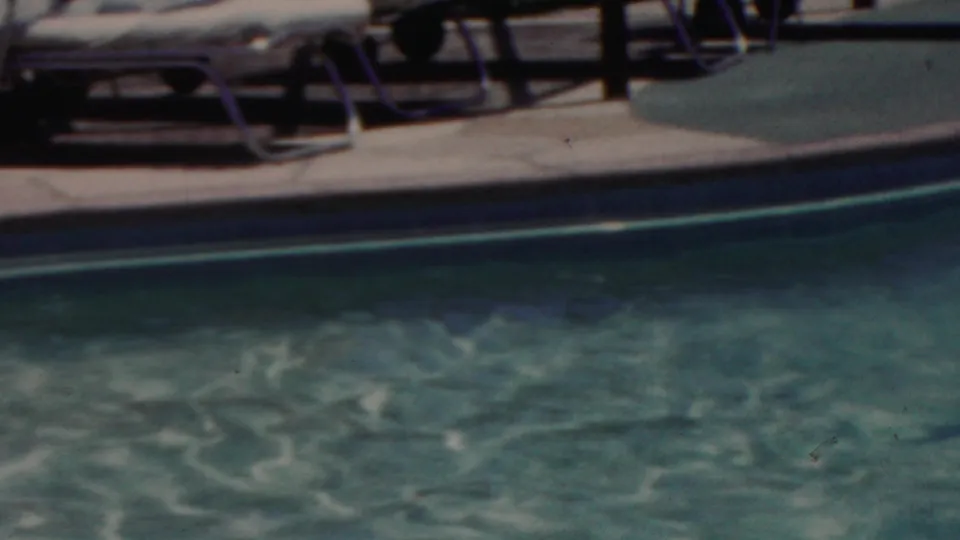Soft 8mm frame from Seaside, New Jersey in 1949 showing turquoise pool water, a curved pool edge, deck paving, and lounge chairs in the background.