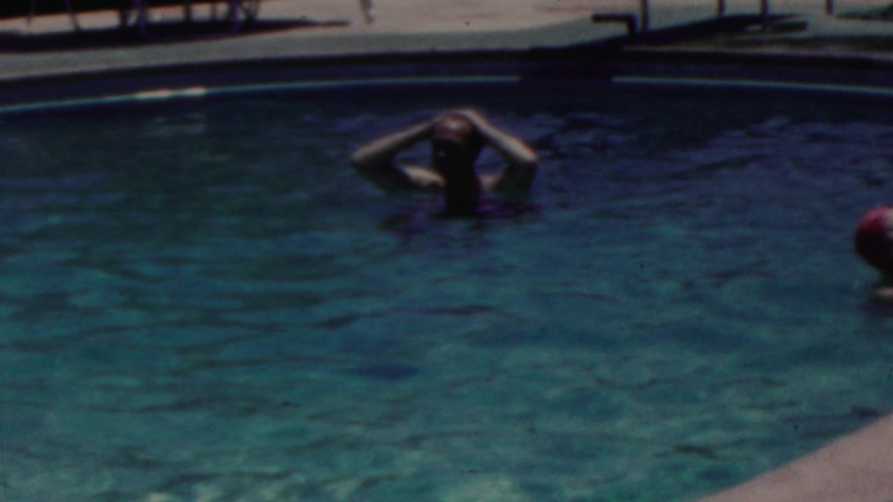 1949 Seaside, New Jersey home-movie frame showing swimmers in blue-green pool water, including one adult relaxing with hands behind the head near the pool edge.