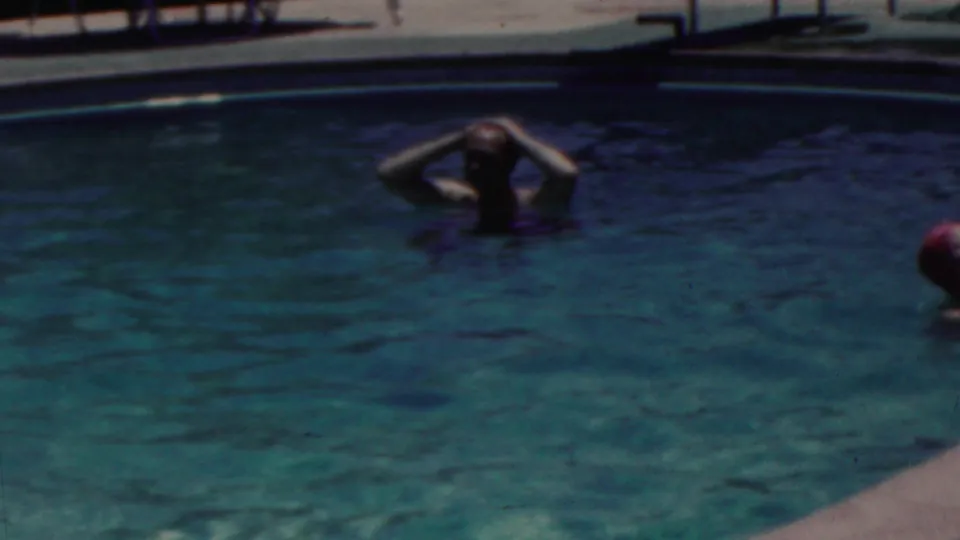 1949 Seaside, New Jersey home-movie frame showing swimmers in blue-green pool water, including one adult relaxing with hands behind the head near the pool edge.