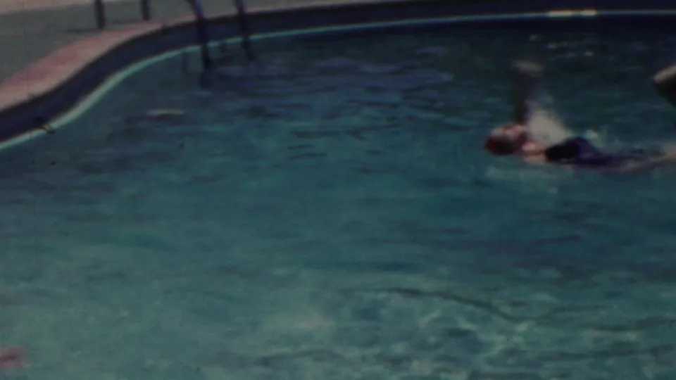 1949 Seaside, New Jersey home-movie frame showing a swimmer crossing the pool near a curved edge, with a metal ladder and sunlit deck visible in the background.
