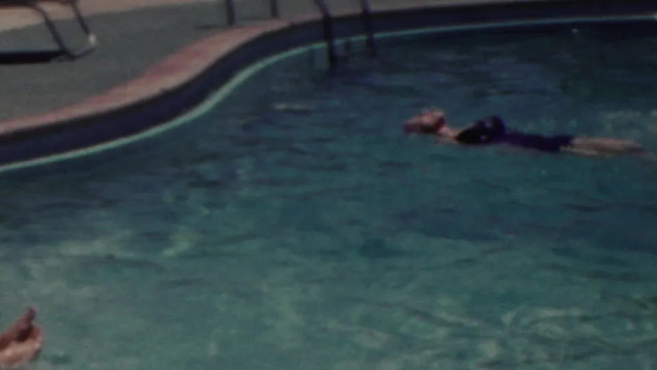 1949 Seaside, New Jersey home-movie frame showing a swimmer stretched out in the water near the curved pool edge, with rippling blue-green water filling the frame.
