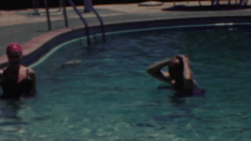 In the 1949 Seaside, New Jersey pool scene, two women wade in the water, one in a pink swim cap and the other raising her hands to her hair.